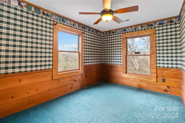 empty room featuring ceiling fan, carpet floors, a textured ceiling, and wood walls