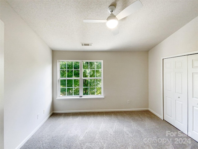 unfurnished bedroom featuring lofted ceiling, light colored carpet, a textured ceiling, a closet, and ceiling fan