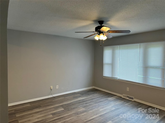 spare room with a textured ceiling, dark wood-style flooring, a ceiling fan, visible vents, and baseboards