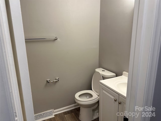 half bathroom with baseboards, visible vents, toilet, wood finished floors, and vanity