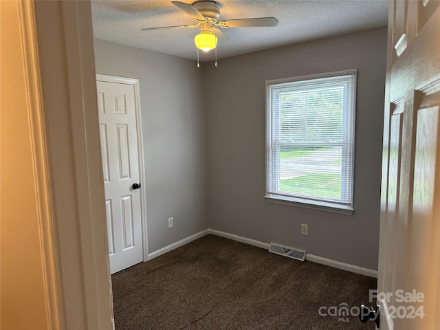 empty room with baseboards, visible vents, dark carpet, and a textured ceiling