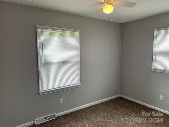 spare room featuring baseboards, visible vents, dark colored carpet, and a ceiling fan