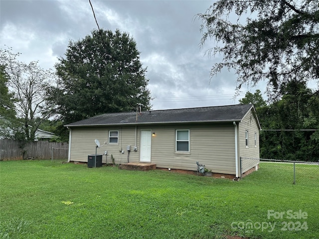 back of property with central air condition unit, fence, and a lawn