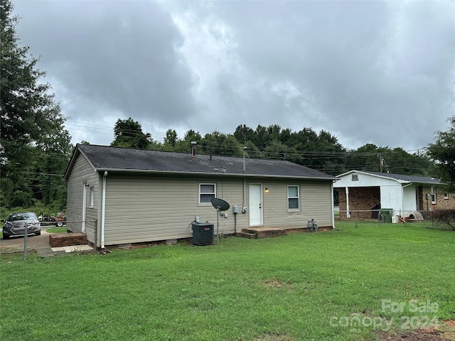 rear view of house featuring a lawn, central AC unit, and fence