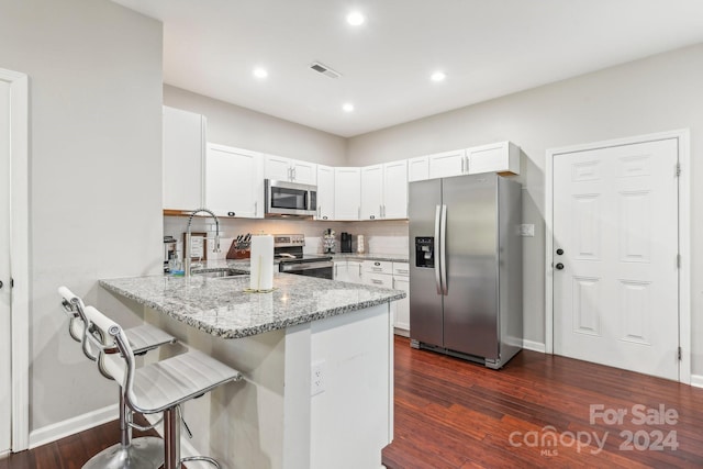 kitchen with stainless steel appliances, dark hardwood / wood-style flooring, white cabinets, light stone counters, and kitchen peninsula