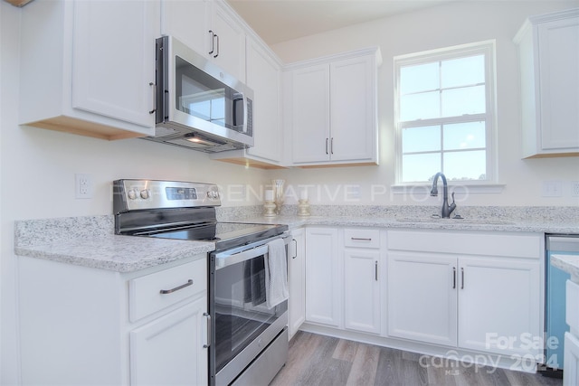 kitchen featuring white cabinetry, light stone counters, light hardwood / wood-style floors, appliances with stainless steel finishes, and sink