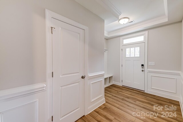 entrance foyer featuring crown molding, a raised ceiling, and light hardwood / wood-style flooring