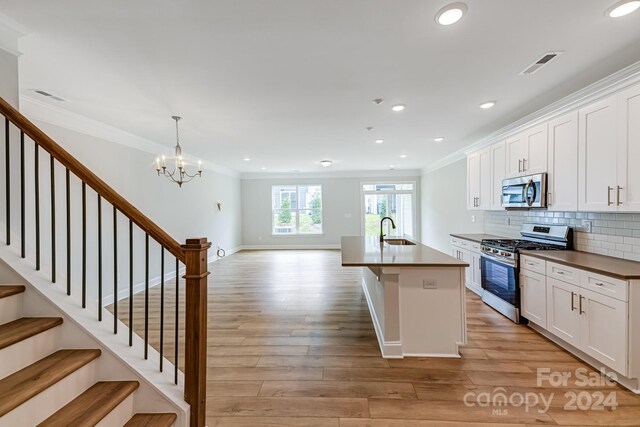 kitchen with appliances with stainless steel finishes, crown molding, sink, white cabinetry, and light wood-type flooring