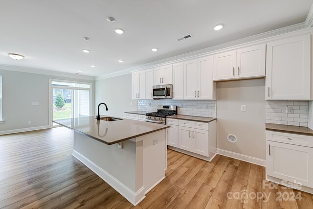 kitchen featuring light hardwood / wood-style flooring, appliances with stainless steel finishes, an island with sink, sink, and white cabinetry