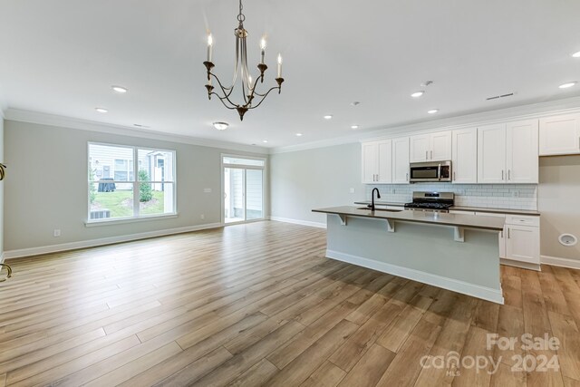 kitchen with appliances with stainless steel finishes, a center island with sink, a notable chandelier, and light hardwood / wood-style floors