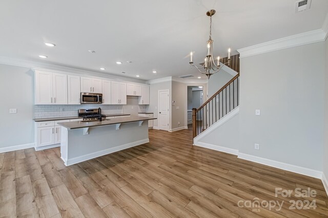 kitchen featuring white cabinetry, stainless steel appliances, an inviting chandelier, an island with sink, and light hardwood / wood-style floors