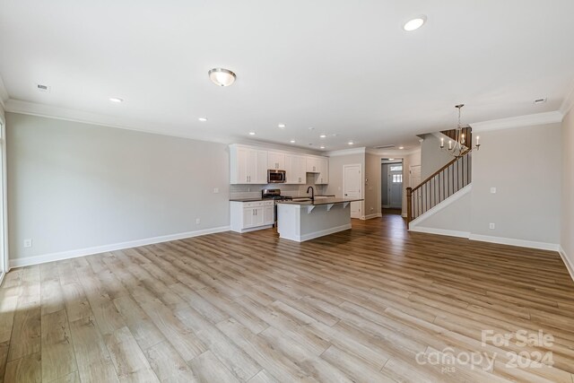 unfurnished living room with crown molding, an inviting chandelier, sink, and light hardwood / wood-style floors