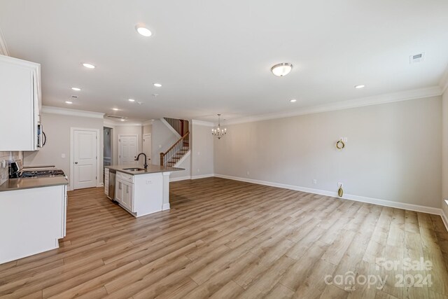 kitchen with white cabinets, light wood-type flooring, a notable chandelier, sink, and a center island with sink