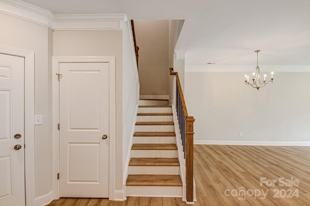 stairway featuring ornamental molding, wood-type flooring, and a chandelier