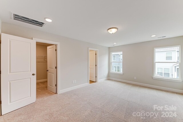 unfurnished bedroom with a walk in closet, light colored carpet, and a closet