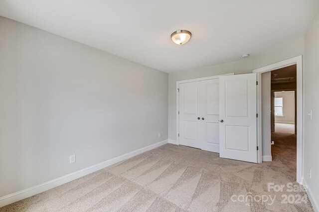 unfurnished bedroom with light colored carpet and a closet