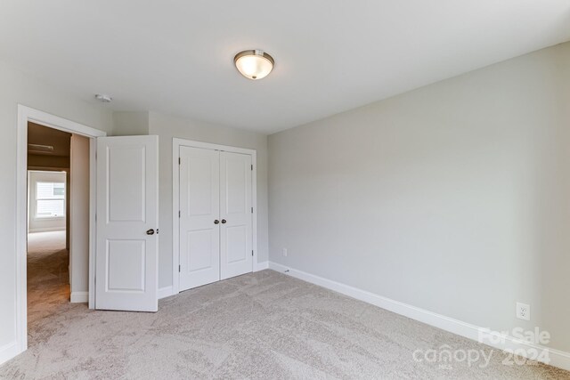 unfurnished bedroom with light colored carpet and a closet