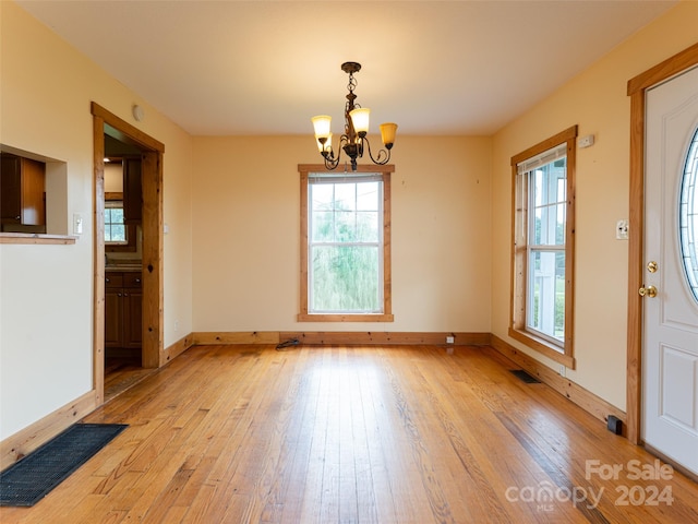 unfurnished dining area featuring a healthy amount of sunlight, a notable chandelier, and light wood-type flooring