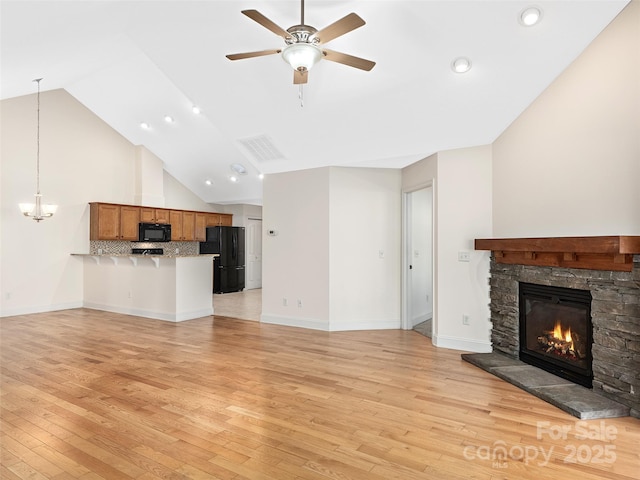 unfurnished living room featuring a stone fireplace, ceiling fan, high vaulted ceiling, and light hardwood / wood-style floors