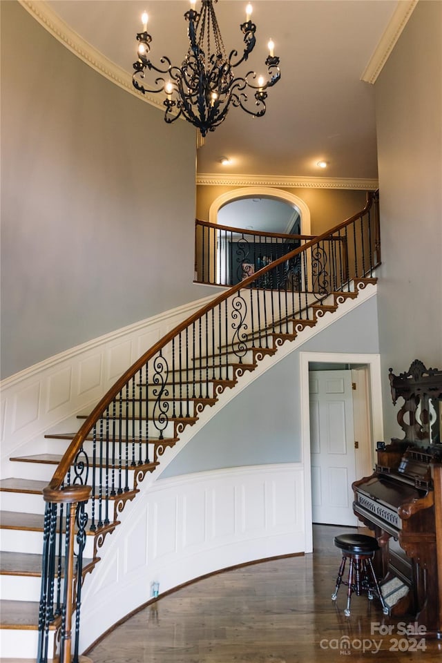 stairs with hardwood / wood-style flooring, crown molding, a chandelier, and a high ceiling