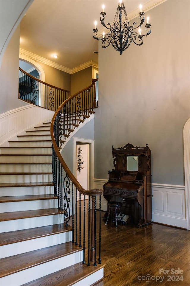 stairway featuring crown molding, hardwood / wood-style flooring, a notable chandelier, and a towering ceiling