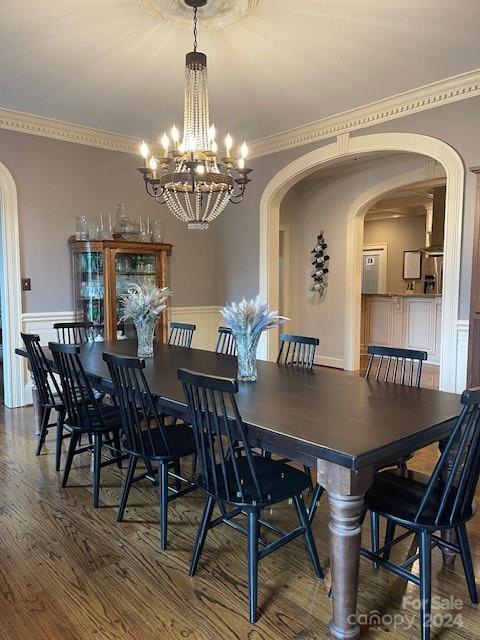 dining space with wood-type flooring, ornamental molding, and a notable chandelier