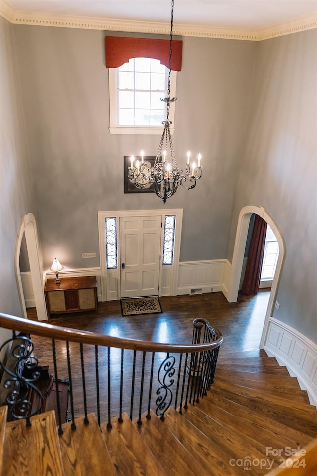 foyer entrance featuring ornamental molding, an inviting chandelier, a wealth of natural light, and dark wood-type flooring