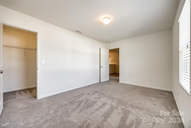 unfurnished bedroom with a walk in closet, a closet, and light carpet