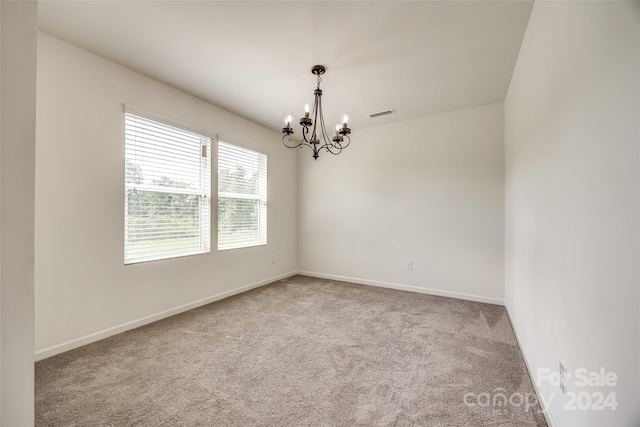 spare room featuring carpet flooring and a chandelier