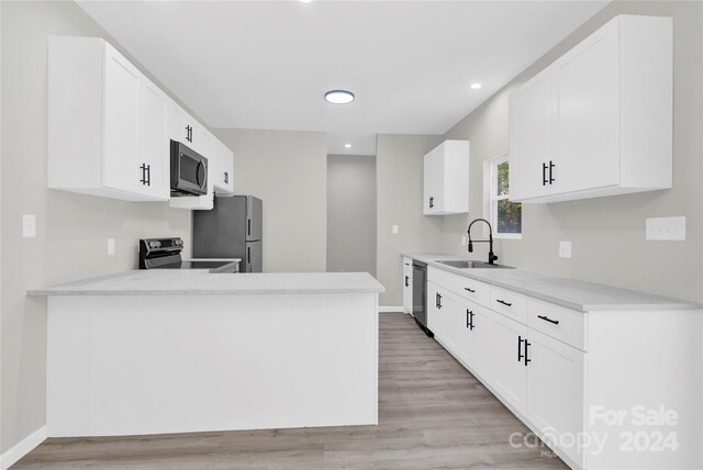 kitchen featuring appliances with stainless steel finishes, sink, light wood-type flooring, white cabinets, and kitchen peninsula