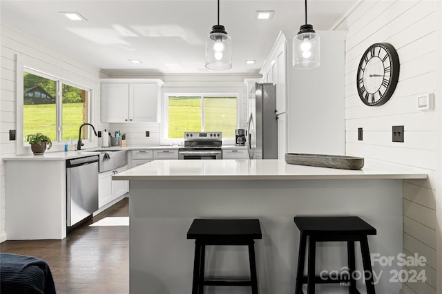 kitchen with sink, white cabinetry, stainless steel appliances, a kitchen breakfast bar, and decorative light fixtures