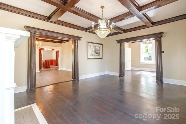 empty room with coffered ceiling, a chandelier, beam ceiling, and ornate columns