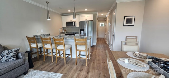 kitchen with white cabinetry, kitchen peninsula, light stone counters, stainless steel appliances, and light hardwood / wood-style floors