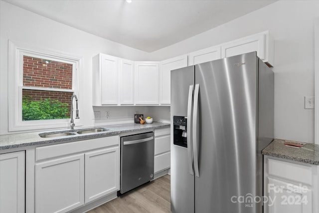 kitchen with appliances with stainless steel finishes, white cabinetry, a sink, and light stone countertops