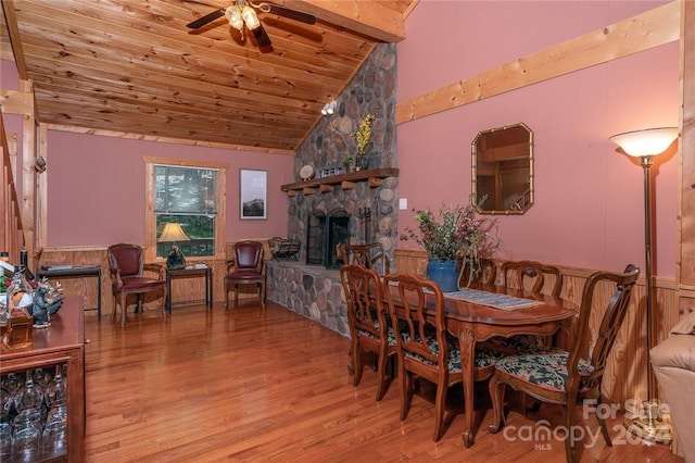 dining room featuring vaulted ceiling, a stone fireplace, ceiling fan, wood ceiling, and light wood-type flooring