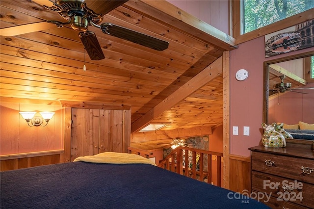 bedroom featuring beamed ceiling, wood walls, a skylight, and wooden ceiling