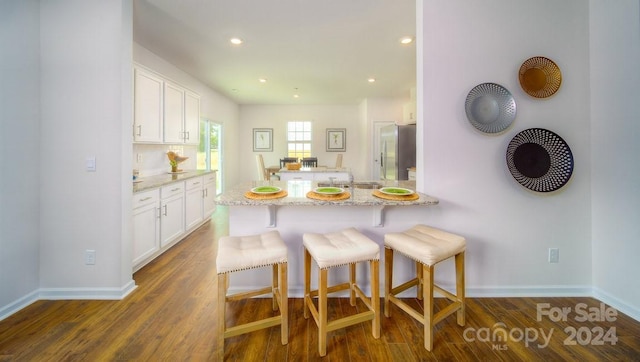 kitchen featuring white cabinetry, a kitchen bar, light stone counters, dark hardwood / wood-style floors, and kitchen peninsula