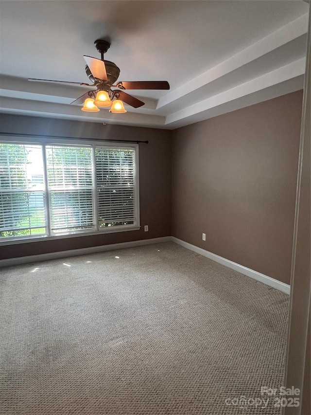 unfurnished room with a raised ceiling, ceiling fan, and carpet