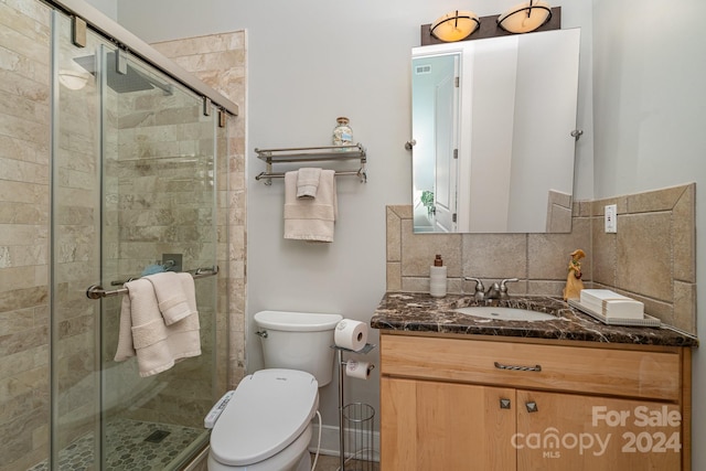 bathroom with toilet, a shower with shower door, vanity, and decorative backsplash