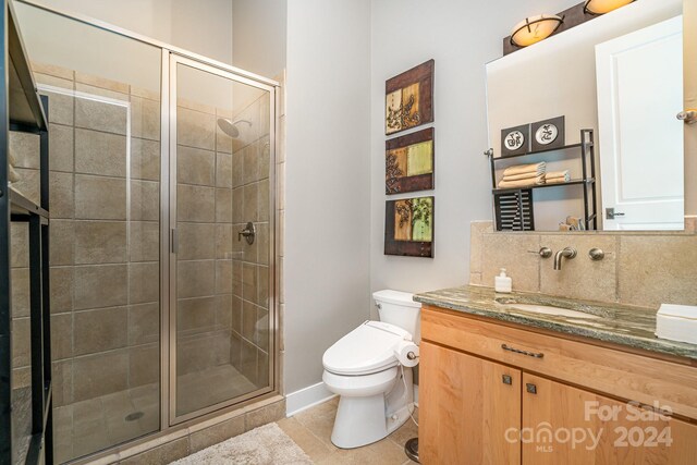 bathroom featuring vanity, tasteful backsplash, a shower with shower door, toilet, and tile patterned flooring