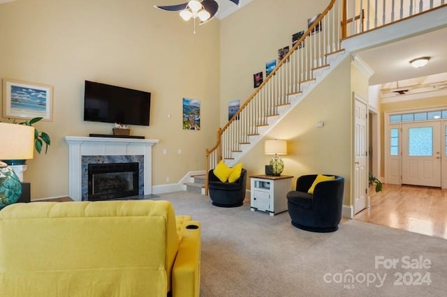 living room with a high ceiling, hardwood / wood-style flooring, a high end fireplace, and ceiling fan