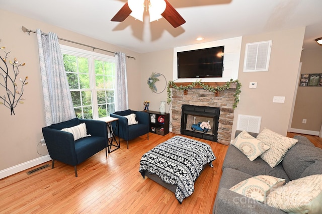 living room featuring hardwood / wood-style flooring, a stone fireplace, and ceiling fan