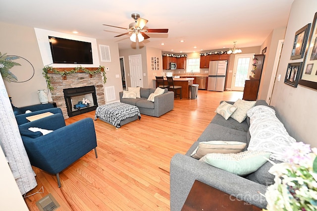 living room featuring a fireplace, ceiling fan with notable chandelier, and light wood-type flooring