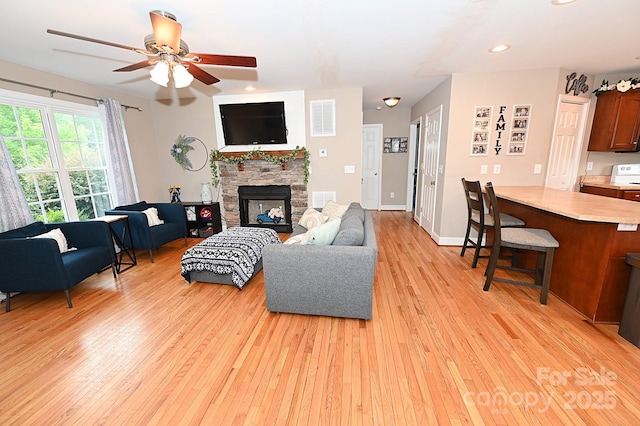 living room with ceiling fan, a stone fireplace, and light hardwood / wood-style floors