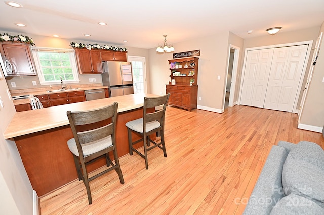 kitchen with a kitchen bar, sink, hanging light fixtures, light hardwood / wood-style flooring, and appliances with stainless steel finishes