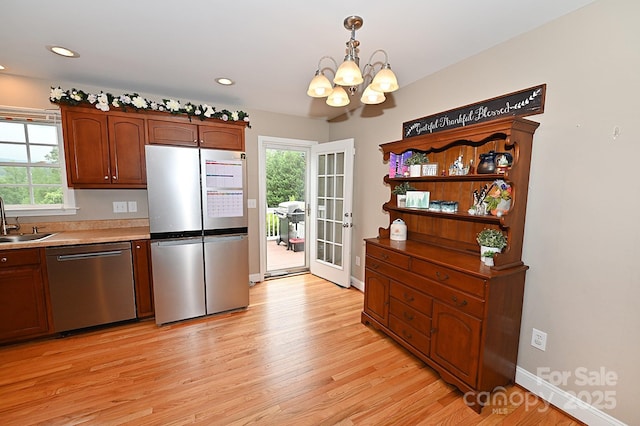 kitchen with decorative light fixtures, sink, a notable chandelier, light hardwood / wood-style floors, and stainless steel appliances