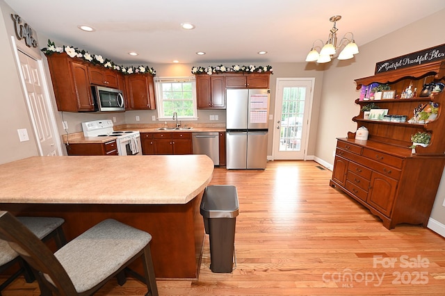 kitchen with sink, appliances with stainless steel finishes, an inviting chandelier, hanging light fixtures, and light hardwood / wood-style floors