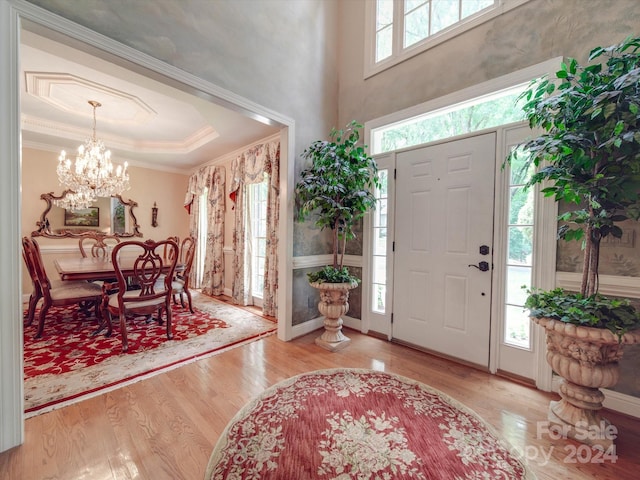 foyer featuring an inviting chandelier, light wood-type flooring, a raised ceiling, and ornamental molding