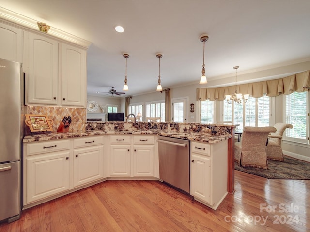 kitchen with decorative light fixtures, appliances with stainless steel finishes, light wood-type flooring, and kitchen peninsula