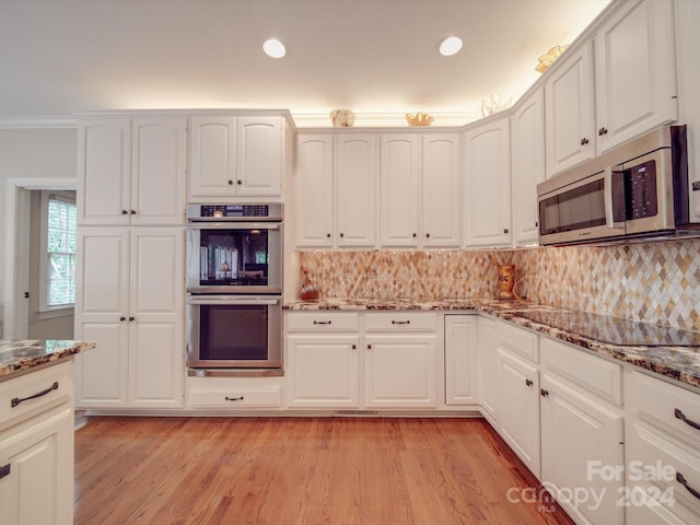 kitchen with appliances with stainless steel finishes, stone counters, light hardwood / wood-style flooring, decorative backsplash, and white cabinetry